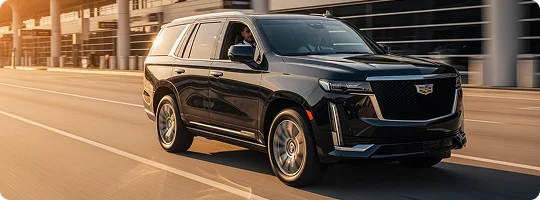 A black Cadillac Escalade in motion driven by a chauffeur and a customer is sitting in front passenger seat while everything in background is in motion blur.