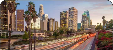 Scenic view along the Los Angeles to Disneyland route showing the downtown skyline at sunset with car light trails on the freeway.