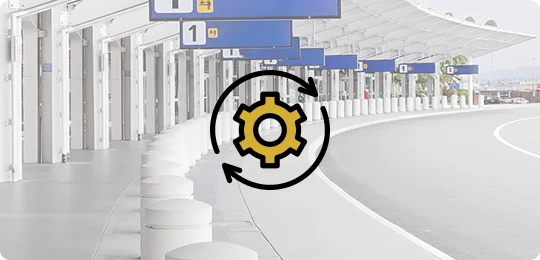 A gold and black graphic of a gear within a circular arrow is overlaid on a slightly blurred photo of an airport curb or drop-off area. The background shows a white, covered walkway supported by pillars, with numbered and labeled signs hanging above the road. The graphic suggests the concepts of efficiency, automation, or continuous service.