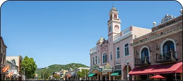 A view of a sunny historic downtown street featuring a large, ornate light-pink building with a tower.