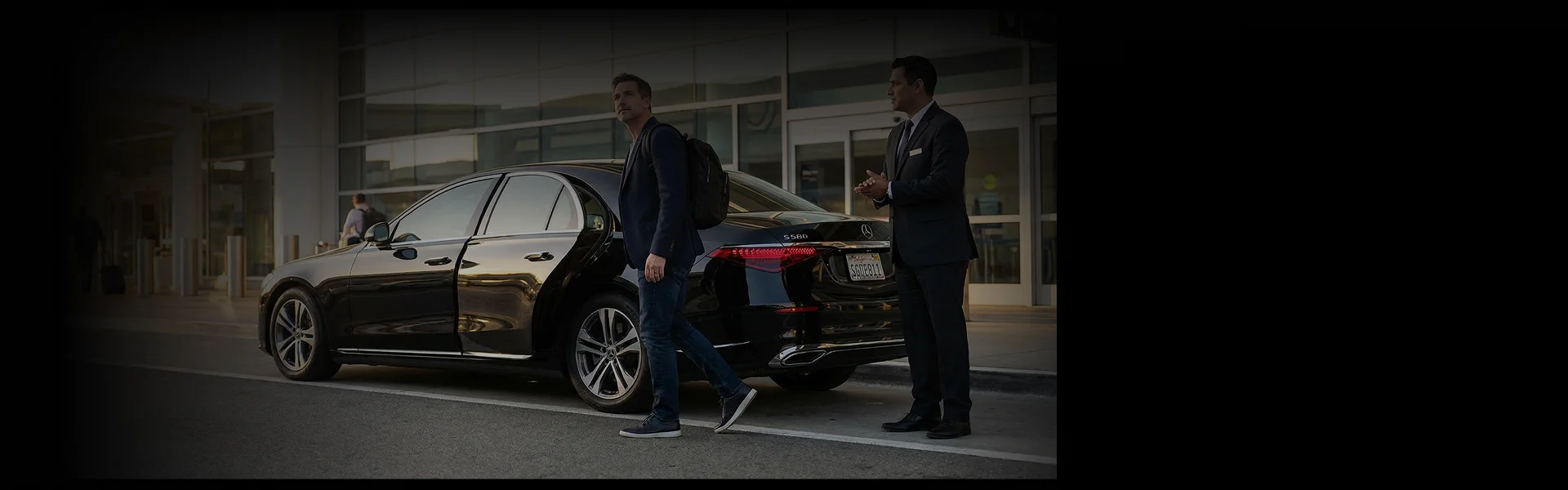 Man with backpack exiting black Mercedes-Benz S560 sedan with chauffeur holding door.